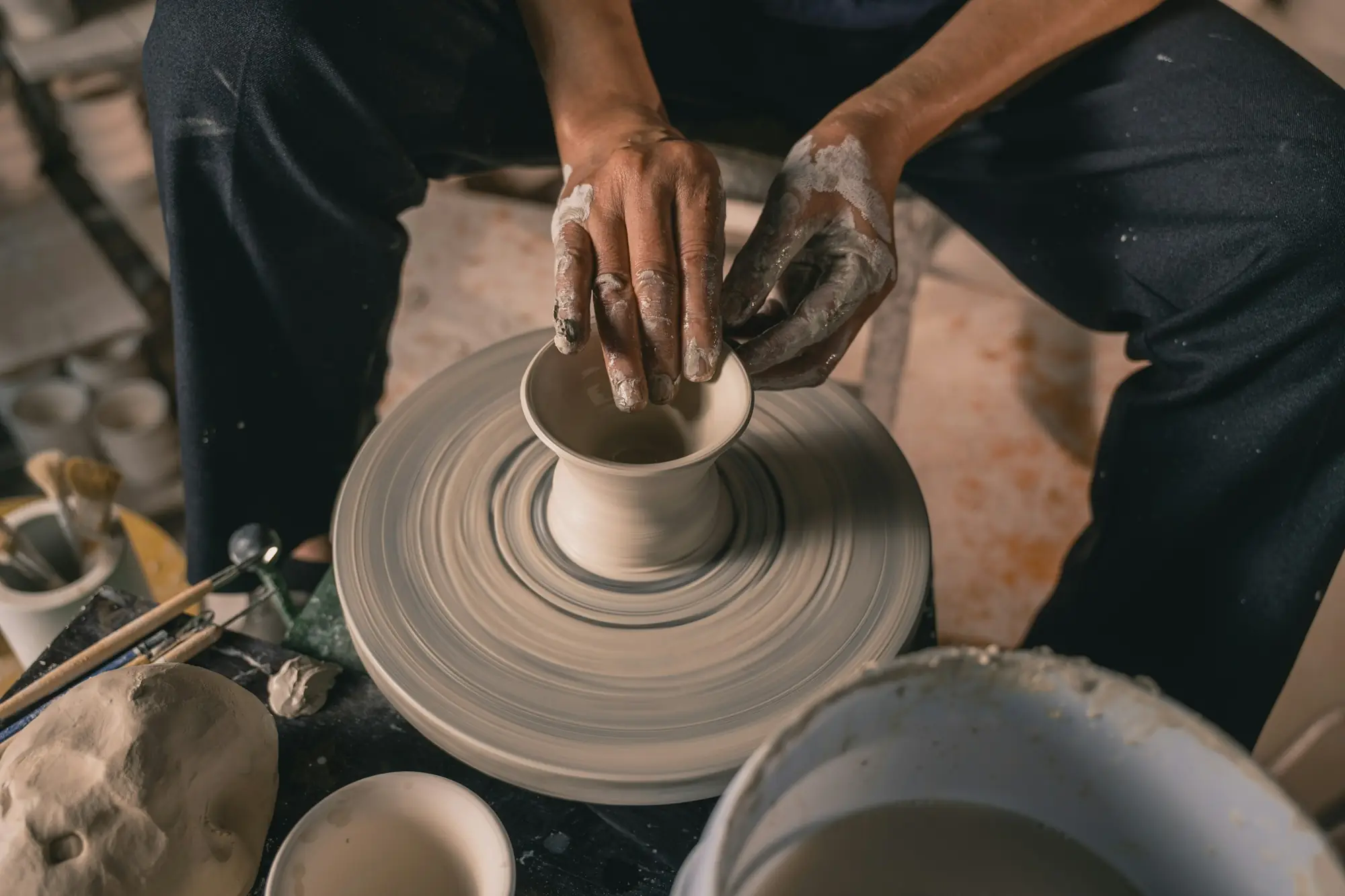 Hands shaping a stoneware bowl on a turning pottery wheel
